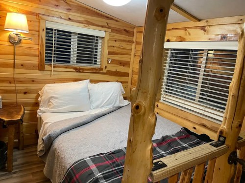 Cozy wooden cabin interior featuring a bed, warm lighting, and large windows with blinds.