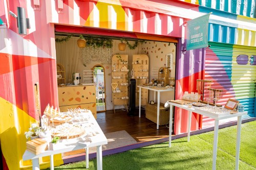 A colorful boutique with jewelry displays and vibrant striped walls, featuring a welcoming entrance and greenery.