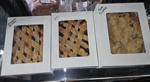 Three boxes of baked goods: a lattice-topped raspberry pie, a cherry pie, and an apple crumble.