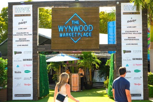 Entrance to The Wynwood Marketplace, featuring event signage and people walking in a vibrant outdoor setting.