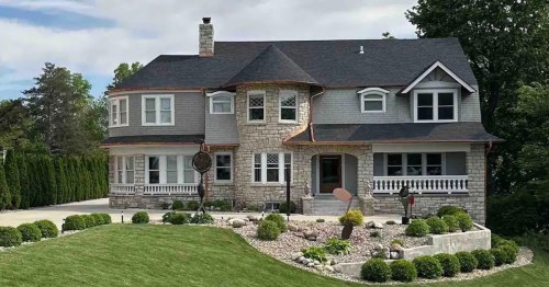 A large, elegant two-story house with a stone facade, manicured lawn, and decorative landscaping.