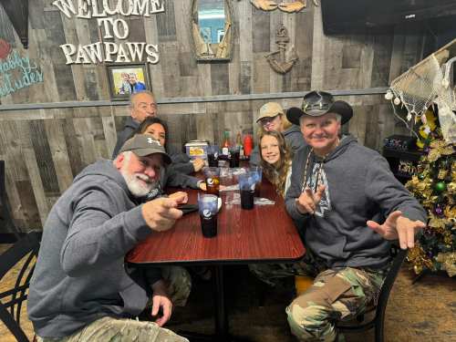A group of six people in casual attire sitting at a table in a cozy restaurant, smiling and enjoying their time together.