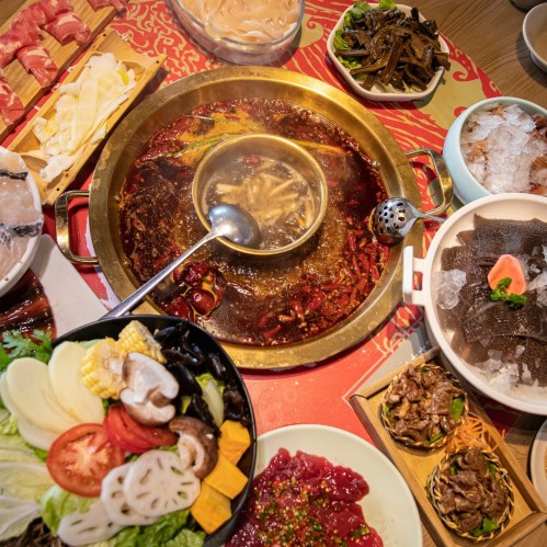 A vibrant spread of hot pot ingredients, including meats, vegetables, and sauces, arranged around a bubbling pot.