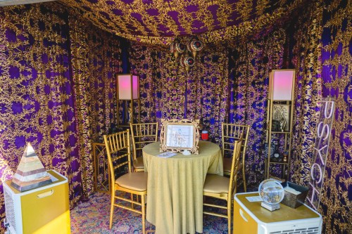 A cozy fortune-telling booth with gold and purple decor, a round table, and chairs, featuring mystical items and a crystal ball.