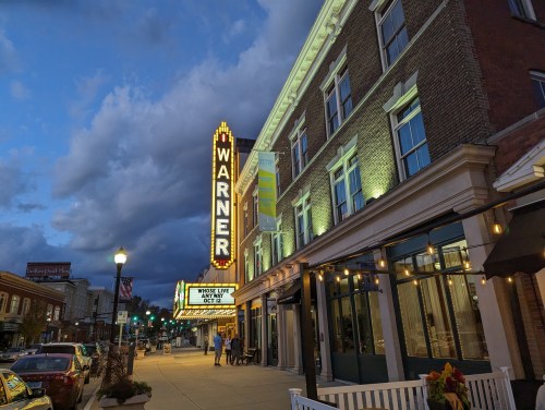 The Warner Theatre illuminated at dusk, showcasing its marquee and charming brick facade.