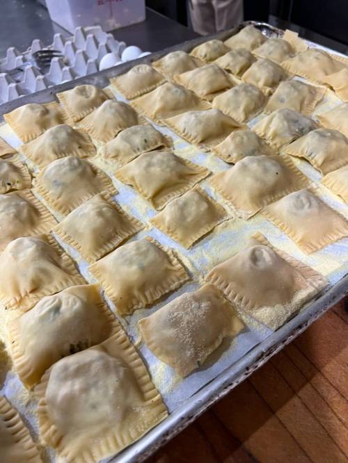 A tray of uncooked ravioli arranged neatly, dusted with flour, ready for cooking.