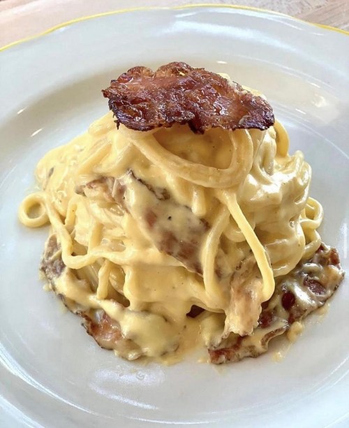 A plate of creamy pasta topped with crispy bacon, served in a white dish.