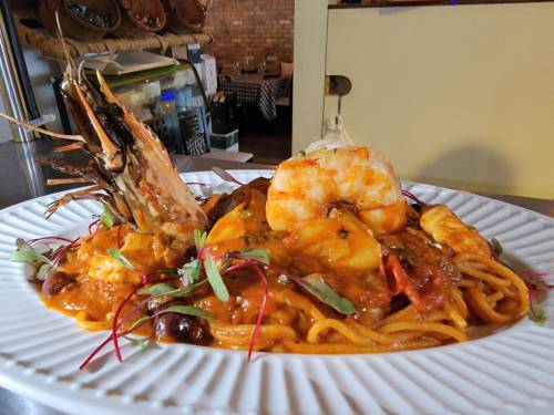 A plate of pasta topped with shrimp and a large prawn, garnished with herbs and a rich sauce.