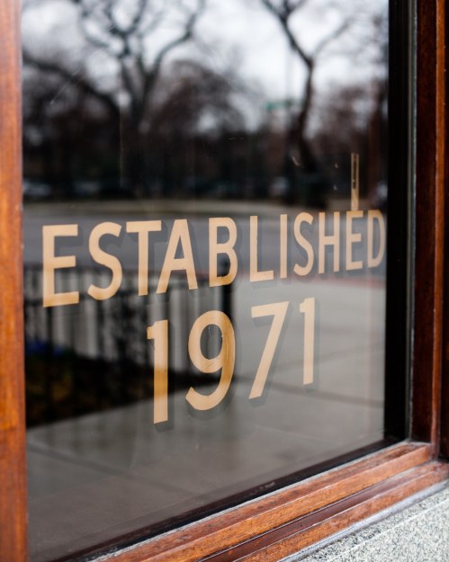 Close-up of a window with the text "Established 1971" etched in gold on a wooden frame.