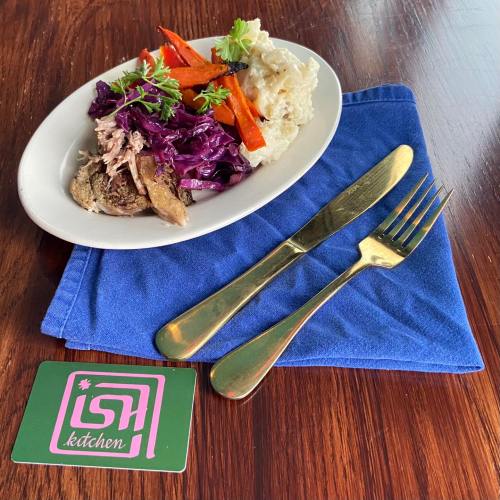 A plate of pulled pork, purple cabbage, carrots, and rice on a blue napkin, with a fork and knife beside it.
