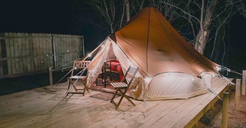 A cozy glamping tent on a wooden deck, illuminated with soft lights, surrounded by trees at night.