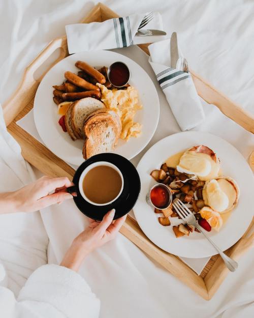 A cozy breakfast in bed featuring eggs, toast, sausage, and coffee on a wooden tray.