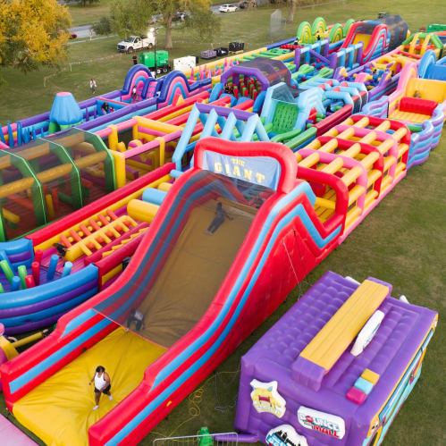 Aerial view of a colorful inflatable playground with slides and obstacle courses set up on a grassy field.