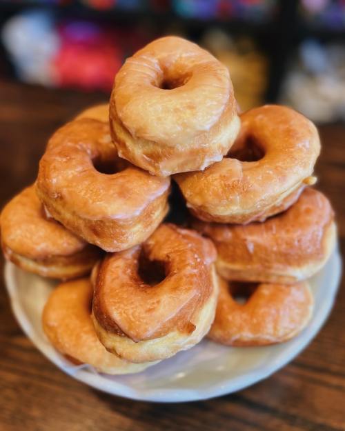 A stack of glazed donuts on a white plate, with a wooden table in the background.
