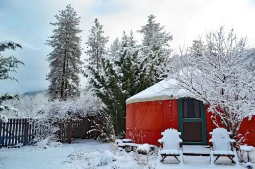 A bright orange yurt surrounded by snow-covered trees and a winter landscape.