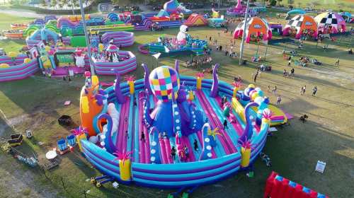Aerial view of a colorful inflatable amusement park with various slides and attractions, filled with people enjoying.