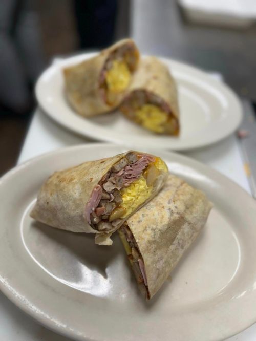 Two burritos filled with eggs, meat, and vegetables, served on white plates.