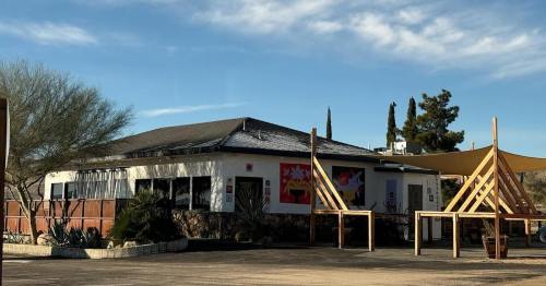 A small, modern building with outdoor seating and desert landscaping under a clear blue sky.