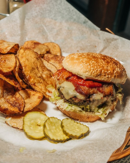A juicy burger with bacon, cheese, lettuce, and tomato, served with crispy potato chips and pickles on the side.
