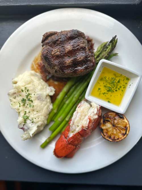 A plate featuring grilled steak, lobster tail, mashed potatoes, asparagus, and a small dish of melted butter.