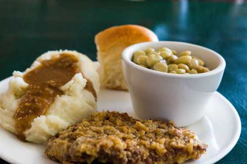 A plate with mashed potatoes topped with gravy, a roll, green beans, and a breaded meat patty.