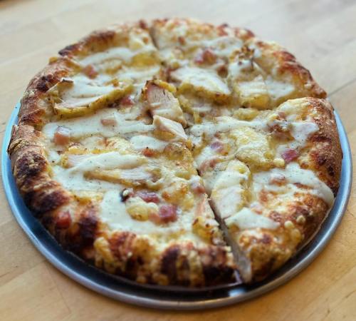 A freshly baked pizza with a golden crust, topped with chicken, cheese, and a creamy sauce, sliced into wedges.