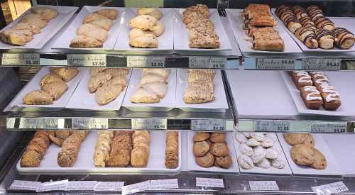 A display case filled with various baked goods, including cookies, pastries, and scones, with price tags visible.