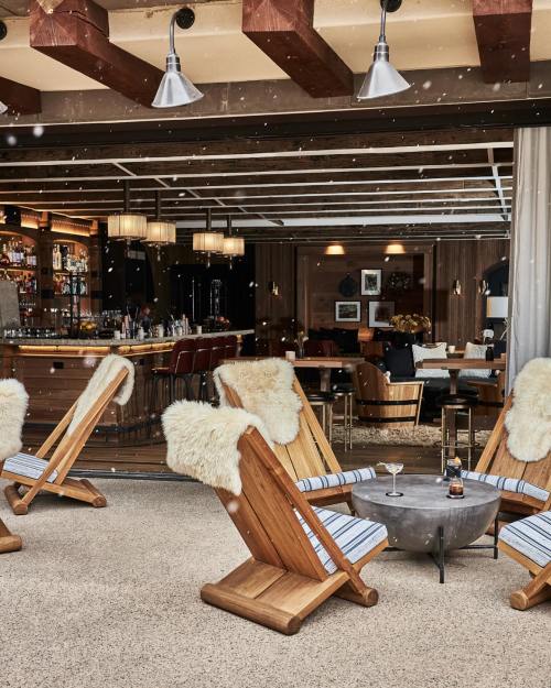 Cozy outdoor seating area with wooden chairs, fur throws, and a small table, set against a stylish bar backdrop.
