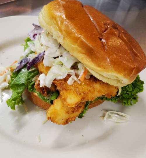A crispy fish sandwich with lettuce, coleslaw, and a soft bun on a plate.