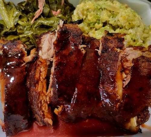A plate featuring sliced barbecue meat, collard greens, and creamy rice, showcasing a delicious Southern meal.