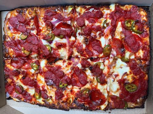 A rectangular pizza topped with pepperoni, jalapeños, and melted cheese in a pizza box.