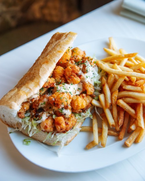 A crispy shrimp sandwich with lettuce and sauce, served with a side of golden French fries.