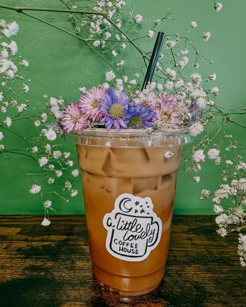 A cup of iced coffee topped with colorful flowers, set against a green background.