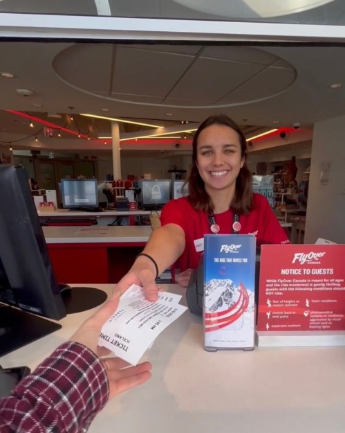 A smiling employee hands tickets to a guest at a ticket counter, with informational brochures in the background.