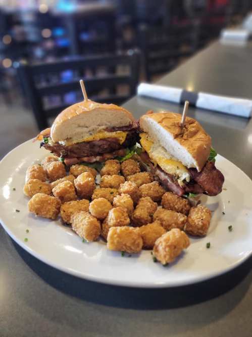 A plate with two burgers topped with bacon and eggs, surrounded by golden tater tots.