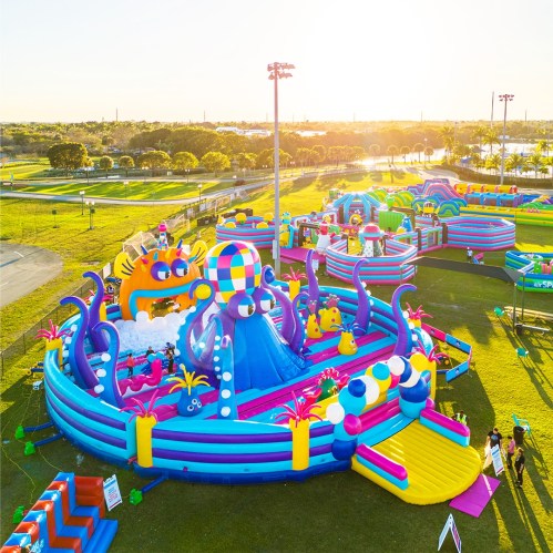 A colorful inflatable water park with slides and play areas, set in a sunny outdoor park.