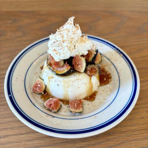 A creamy dessert topped with whipped cream, fresh figs, and a drizzle of caramel on a blue-rimmed plate.