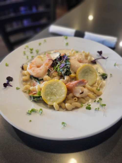 A plate of creamy pasta with shrimp, lemon slices, and microgreens, garnished with fresh herbs.