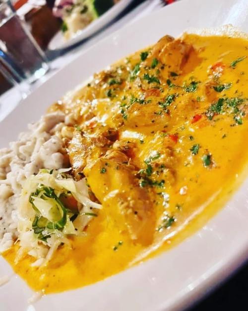 A plate of creamy chicken curry served with rice and a side of fresh salad, garnished with herbs.