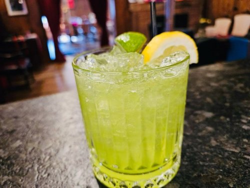 A vibrant green cocktail with ice, garnished with a lime and lemon slice, served in a textured glass.