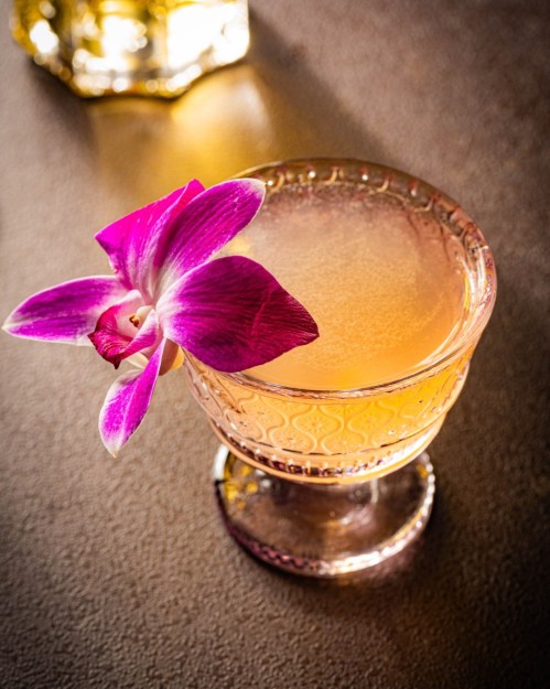 A beautifully crafted cocktail in a decorative glass, garnished with a vibrant purple orchid flower.