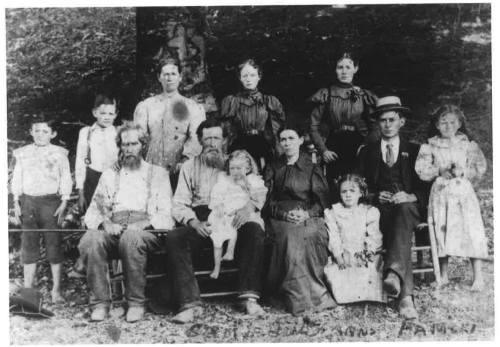 A black and white photo of a large family group, seated and standing together outdoors, dressed in early 1900s clothing.