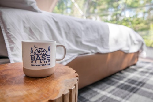 A cozy interior with a mug on a wooden table, a bed in the background, and natural light filtering through.