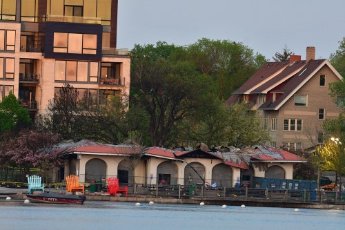 A lakeside view featuring colorful chairs, a damaged building, and modern apartments in the background.