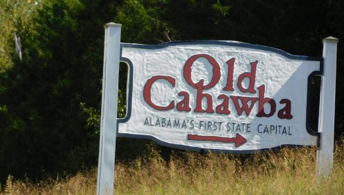 Sign for Old Cahawba, Alabama's first state capital, with an arrow pointing to the right, surrounded by tall grass.