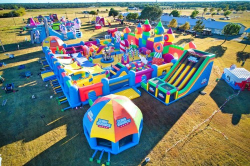 Aerial view of a colorful inflatable bounce park with various slides and obstacles set in a grassy field.