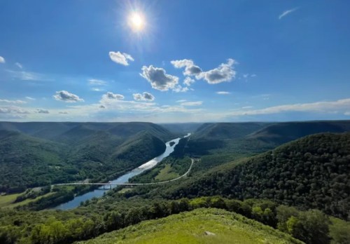 A scenic view of a winding river surrounded by lush green hills under a bright blue sky with fluffy clouds.