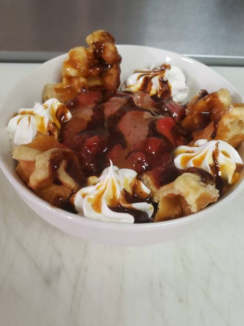 A bowl of dessert featuring ice cream, whipped cream, chocolate syrup, caramel, and waffle pieces.