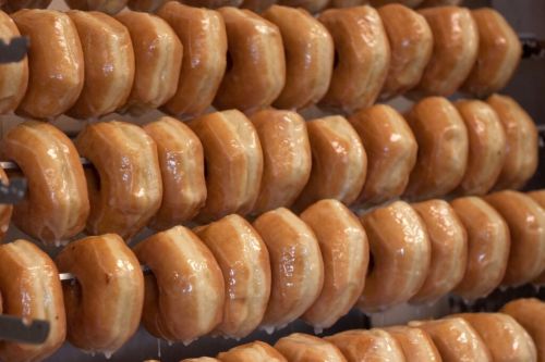 A close-up of freshly glazed donuts arranged on a rack, showcasing their shiny, golden-brown surface.