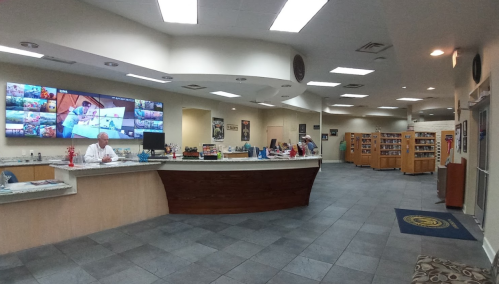 A spacious reception area with a front desk, large screens, and shelves filled with books in a well-lit environment.